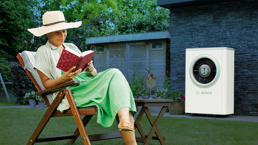 a person sitting and reading a book in their garden with air to heat source renewables machine in the background